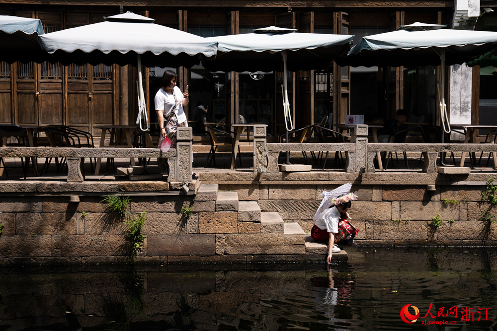 5月26日，在浙江省嘉興市月河街，一位母親給正在俯身戲水的孩子拍照。人民網記者 葛泰佚攝