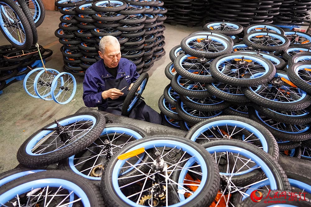 在浙江省慈溪市觀海衛鎮一童車企業，工人在生產線上安裝飛輪。人民網 章勇濤攝